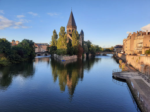 Auf einer Insel in einem Fluss steht eine große Kirche. Auf der Insel wachsel hohe Bäume.