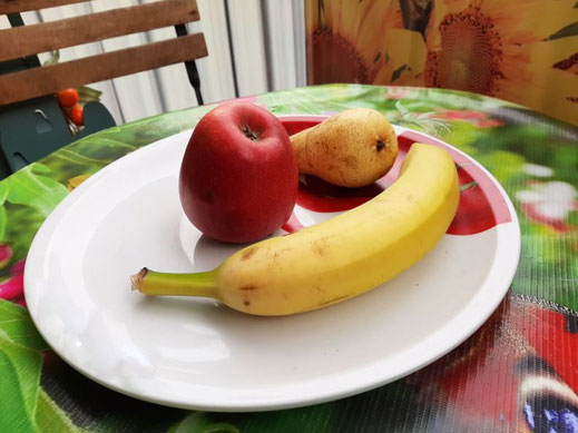 ein Apfel, eine Birne und eine Banane liegen auf einem Obstteller