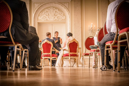 Das Brautpaar sitzt während der Hochzeit am Trautisch vor der Traurednerin.