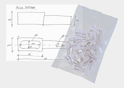 Zu sehen eine Handskizze einer Endkappe mit Bemaßungen. Leicht überlappend liegt auf ihr eine Tüte mit lauter 3D-gedruckten Endkappen in Weiß die der Handskizze entsprechen.