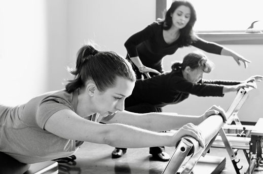 Comprehensive Rehab-Certified Instructor guiding two clients with back tightness to improve their posture and relieve stress on Pilates Pro Reformer at STUDIO ORIGIN customized Pilates in Yamhill County Oregon.