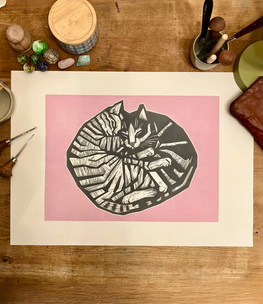 Linoldruck von zwei kuschelnden Katzen in schwarz mit rosafarbenem Hintergrund.
