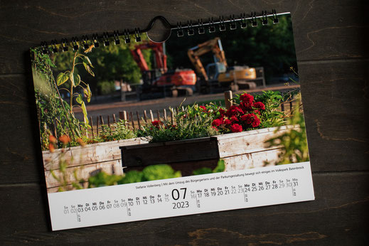 Stadtteilkalender Batenbrock, aufgeschlagen, Monat Juli, Bild von Stefanie Vollenberg, bepflanzte Hochbeete im Vordergrund, Bagger im Hintergrund