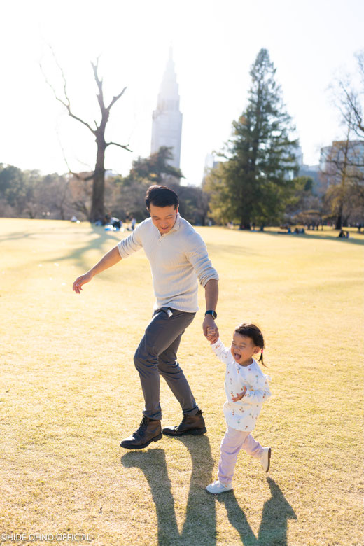 First family memories in Japan — Father and daughter running hand in hand in Shinjuku Gyoen, joyful moments from their first trip to Tokyo.