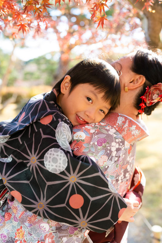 Smiling boy in kimono hugging his mother under autumn leaves in Asakusa, Tokyo