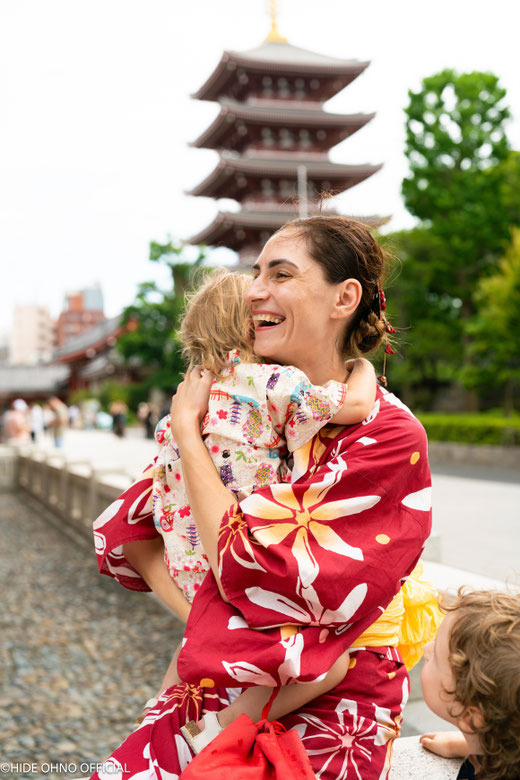 Mother in red kimono holding child and smiling in front of Senso-ji temple in Asakusa, Tokyo