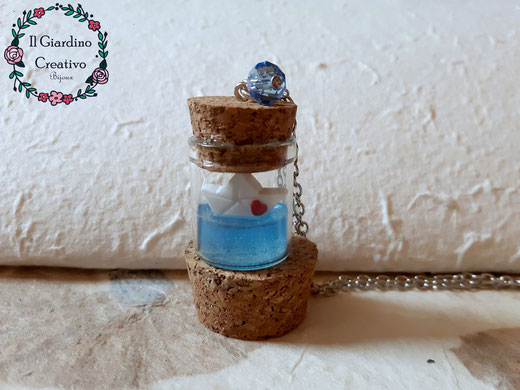 Collana Barchetta di carta modellata a mano, che naviga su un mare azzurro realizzato in resina, dentro un barattolino di vetro con tappo in sughero