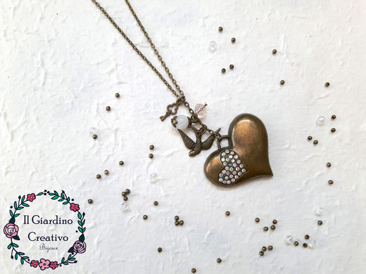  Collana "Cuore romantico" realizzata con pendente cuore in metallo color bronzo antico con strass, ciondolo rondine, chiave e perline in resina e in vetro.  Misura: lunghezza 67cm