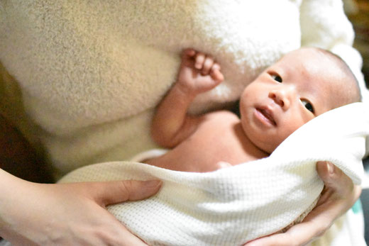 母親に抱っこされる男の子の赤ちゃん。ニューボンフォトの撮影は初めてでドキドキします。と言っている気がします。