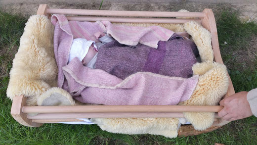 2 handgewebte Decken für eine Babywiege aus dem Mittelalter, das Baby in der Wiege schläft ganz fest, die Mütze ist über sein Gesicht gerutscht