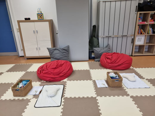 Kursaufbau im Familienbüro Lustadt, rote Sitzsäcke, graue Kissen, waschbare Wickelunterlagen, Wickeldummies auf den Unterlagen und Körbchen mit Stoffwindeln