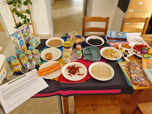 Kursaufbau im Familienbüro Bellheim, Teller mit verschiedenen Lebensmittel, Bücher, Gläschen und Babyprodukte verschiedener Firmen wie Hipp, dm Bio, Bebivita