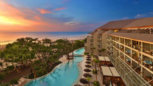 Hôtel élégant en bord de plage avec piscine et vue sur l’océan au coucher du soleil doré.