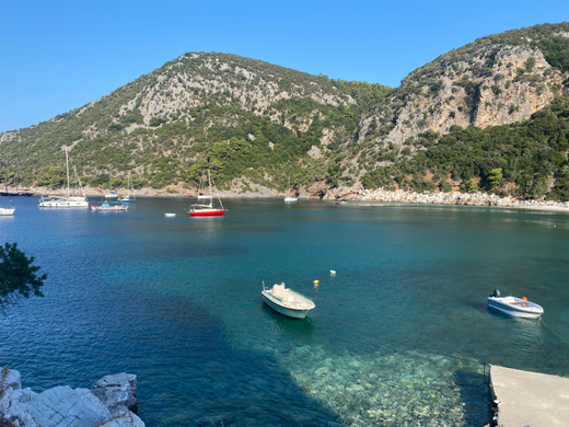 spiaggia du Skopelos con mare cristallino e rocce bianche e pineta sullo sfondo e barchette nel mare