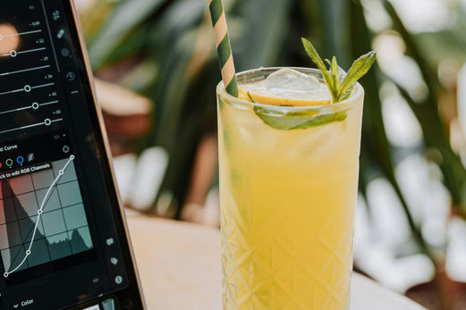 黒のタブレット。ドーナッツとコーヒー。卓上サイズの観葉植物。リングノートのうえに置かれたボールペンとサングラス。