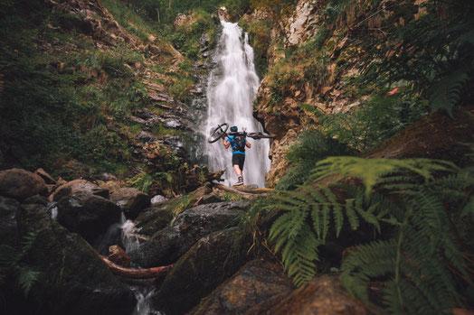 Ein Mann schultert sein Cannondale Trail Neo am Wasserfall