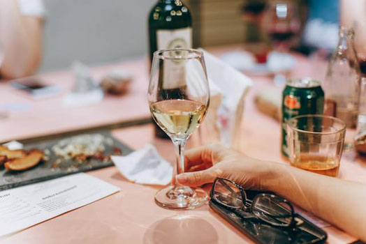 桜の木の下でビールの入ったプラカップと三色団子を両手に持つスーツ姿のビジネスパーソン。会社主催の花見。
