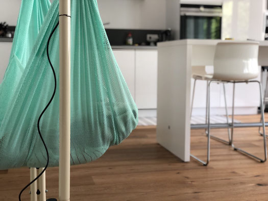 Federwiege steht auf Holzboden in weißer Küche mit Bartisch und Stühlen Baby macht Mittagsschlaf in der Wippe