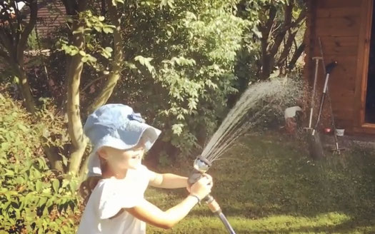 Mädchen im Garten was mit einem Wasserschlauch eine Wasserfontäne erzeugt, um sich von der Hitze abzukühlen