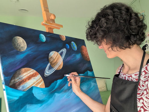Person malt an einer Staffelei ein Acrylbild mit Planeten und Sternenhimmel