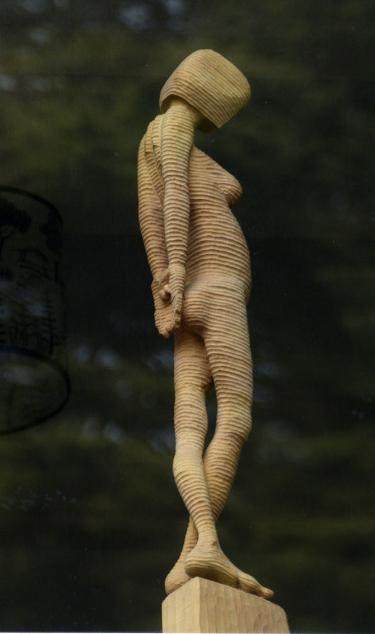 My Lime Woman sculpture, seen from below and through glass with reflected trees. 