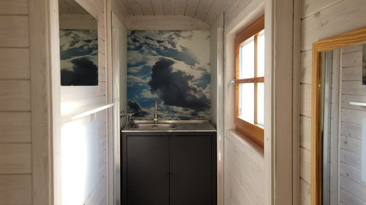 Spülbecken in Holzwagen mit Wolken-Motivhintergrund.