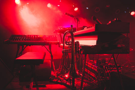 Trompete auf Bühnenständer im roten Bühnenlicht, Synthesizer und Mikrofone im Hintergrund, Nebelmaschine – Konzertfotografie Sebastian Bisch, Wolfsburg.