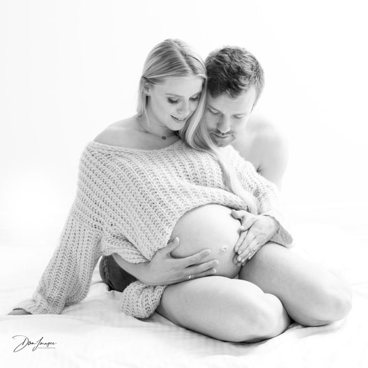 Photo d'un couple assis sur le sol du studio regardant le ventre arrondi pendant une séance photo de grossesse