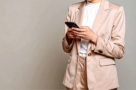 スマホで求人サイトをチェックするジャケット＆パンツ姿の女性。