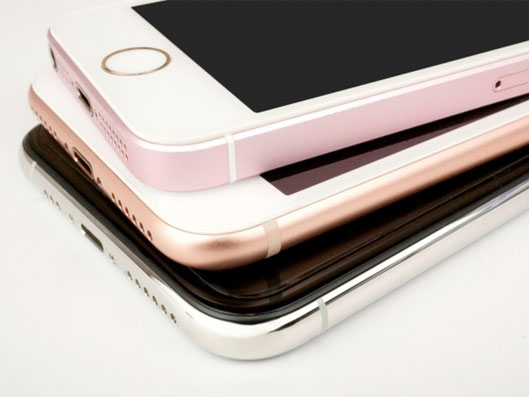 白やピンク、黒、シルバーの複数のiPhoneが重ねて置かれている写真。iPhone修理、画面割れ修理、バッテリー交換、水没修理、充電不良などの案内に関連する端末写真。