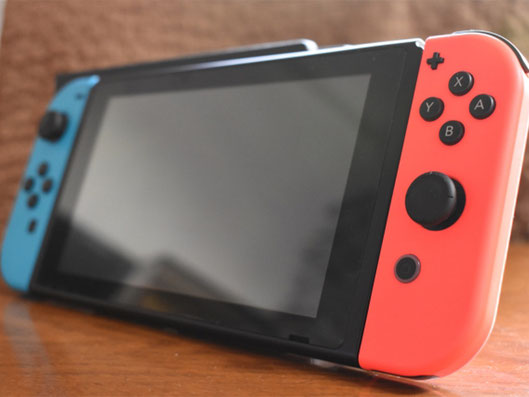木目のテーブルの上に、青と赤のJoy-Conを装着したNintendo Switch本体が置かれている写真。Switch修理、画面修理、バッテリー交換、Joy-Con修理に関連する端末イメージ。