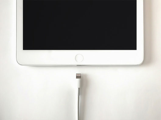 白いiPadの下部と、すぐ下に置かれたLightning充電ケーブルの先端が写っている写真。iPadのバッテリー交換、充電不良、電池の減りが早い症状に関連する状態イメージ。
