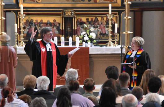 Pfarrer Markus Heßler und Pfarrerin Merle Blum predigen vor dem Altar mit den Taufkerzen.