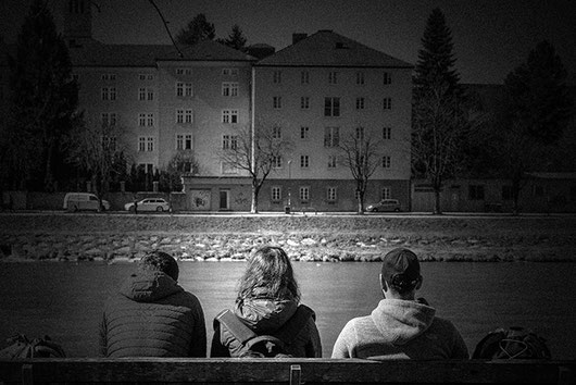 2020-03-13: A group of 3 men is sitting on a bench on the banks of the river Salzach