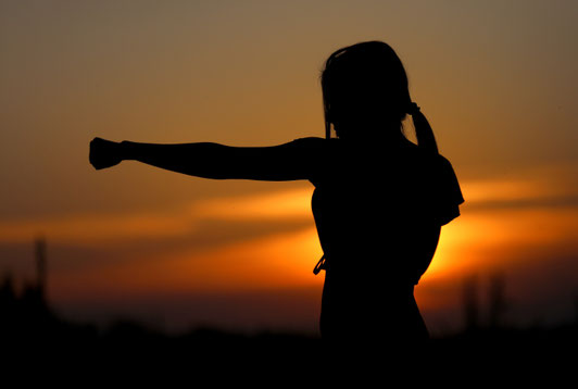 Silhouette einer Frau vor einem Sonnenuntergang, die einen Karateschlag ausführt.