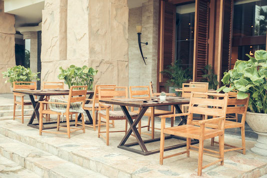 カフェの外観。オープンテラスが設置されている。木製のテーブルと椅子。グリーンの鉢植え。