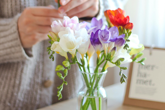 オフィスのテーブルに花を飾るセーター姿の女性。ガラスの花瓶にクロッカスの花。