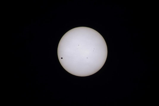 太陽の前をゆっくりと通り過ぎる金星。6時間ほどかけて、左下から右上に向かいゆっくりと横切る姿が石垣市でも確認できた。左下が金星、中心部の点は黒点=6日午前8時(写真家・安田雅弘氏提供)