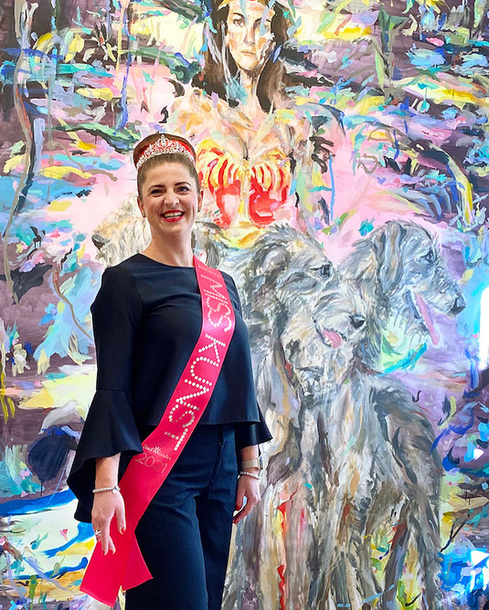 Die Künstlerin Zoë MacTaggart als Miss Kunst vor einem farbenfrohen Gemälde