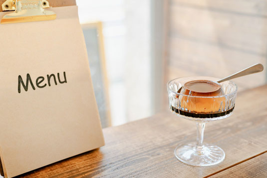 カフェのテーブルに置かれたメニュー。プリンが盛り付けられたガラスの器とスプーン。
