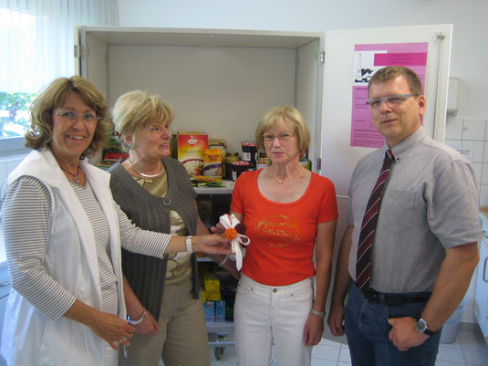 Auf dem Foto sehen Sie Iris Müller (2. von li.) und Petra Ensberg vor dem Lebensmittelschrank der Essensbank bei der Geldübergabe an Frau Höhl und Herrn Pfarrer Beuthert.