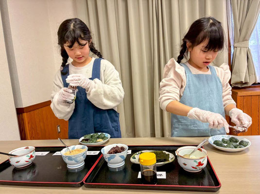 2人の日本人の子供が、つきたてのよもぎ餅にお好みのトッピング具材を楽しそうに盛り付けしている、微笑ましい体験風景。