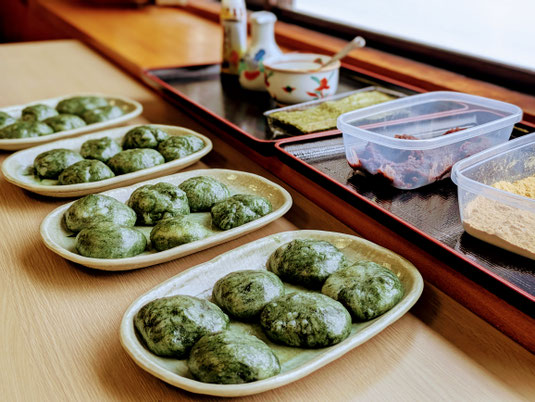 よもぎ餅つき体験の食事会で、お皿に美しく盛り付けられたよもぎ餅を手前に配置し、背景にきなこやあんこ、えごまなどの色鮮やかなトッピング具材が並んでいるシズル感のあるカット。