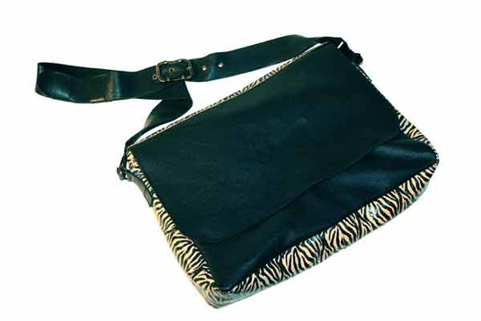 Cette photo représente le sac Ernestine, nouvelle création de maroquinerie aux Sabots d'Isa, une grande besace en cuir noir et cuir zébré, avec des mousquetons noirs et une grosse boucle de ceinture en laiton vieilli.