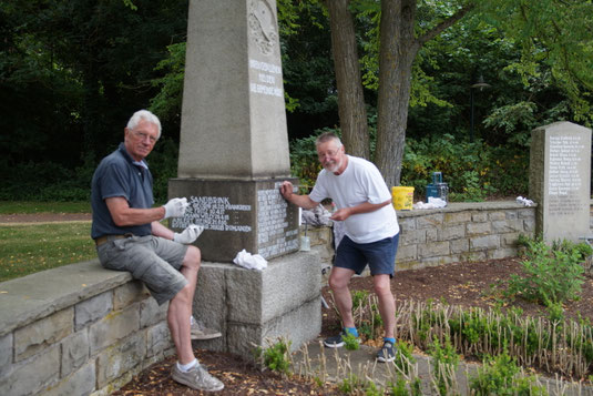2 Männer arbeiten mit Pinseln an einem Kriegsdenkmal.