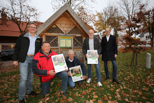 5 Männer, stehend und kniend vor einem Insektenhotel, drei halten ein Plakat in den Händen.