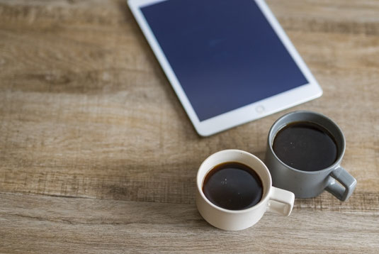 デスクに置かれたタブレット。2つ並んだコーヒーのマグカップ。