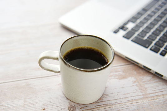 ノートパソコンの傍らに置かれたコーヒーのマグカップ。