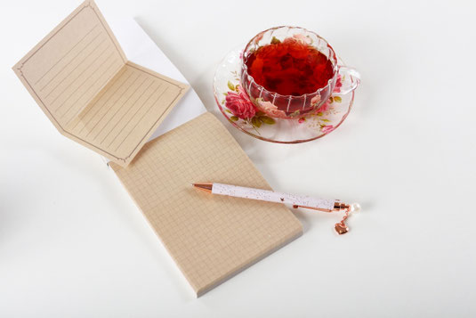 方眼紙のメモパッドとボールペン。紅茶のはいった花柄のカップ&ソーサ。