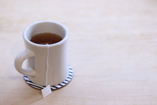 紅茶のティーパックが入れられた白色のマグカップ。ストライプ模様のコースター。